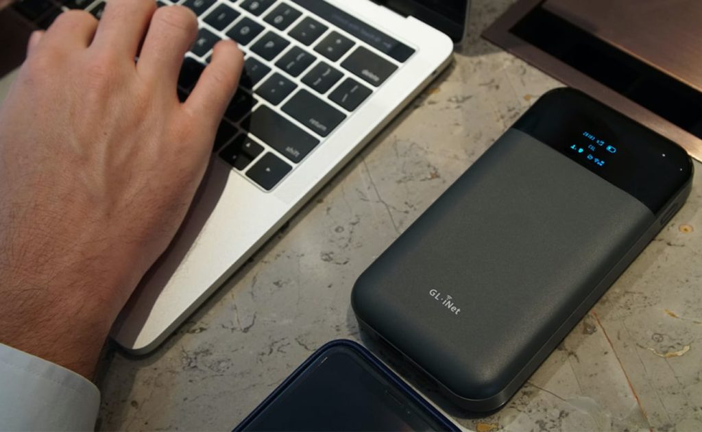  شخصی که در حال نوشتن یک لپ تاپ است ، و یک روتر حریم خصوصی روی میز کنار آن. 